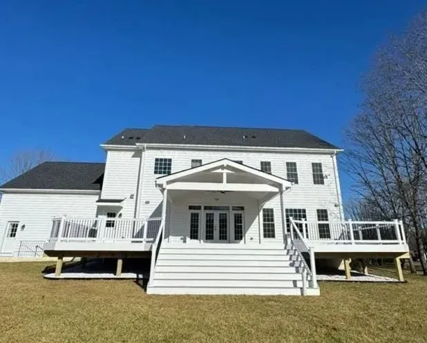 White two-story house with a porch and deck, set against a clear blue sky.