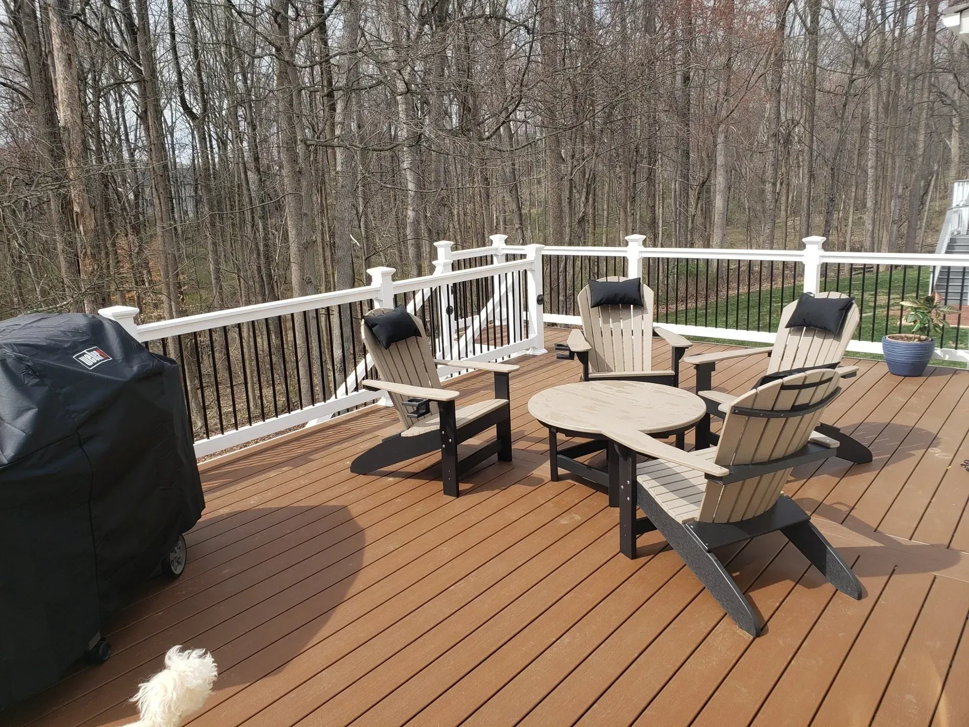 A deck with a grill and outdoor furniture overlooks a wooded area.