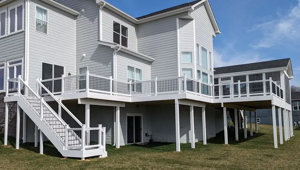 Two-story gray house with white deck and stairs on a sunny day.