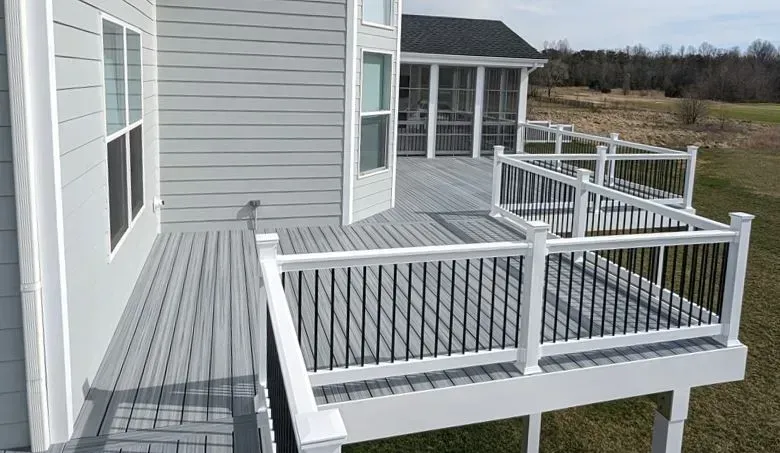 Gray deck with white railing next to a light gray house.  A screened porch is in the background.