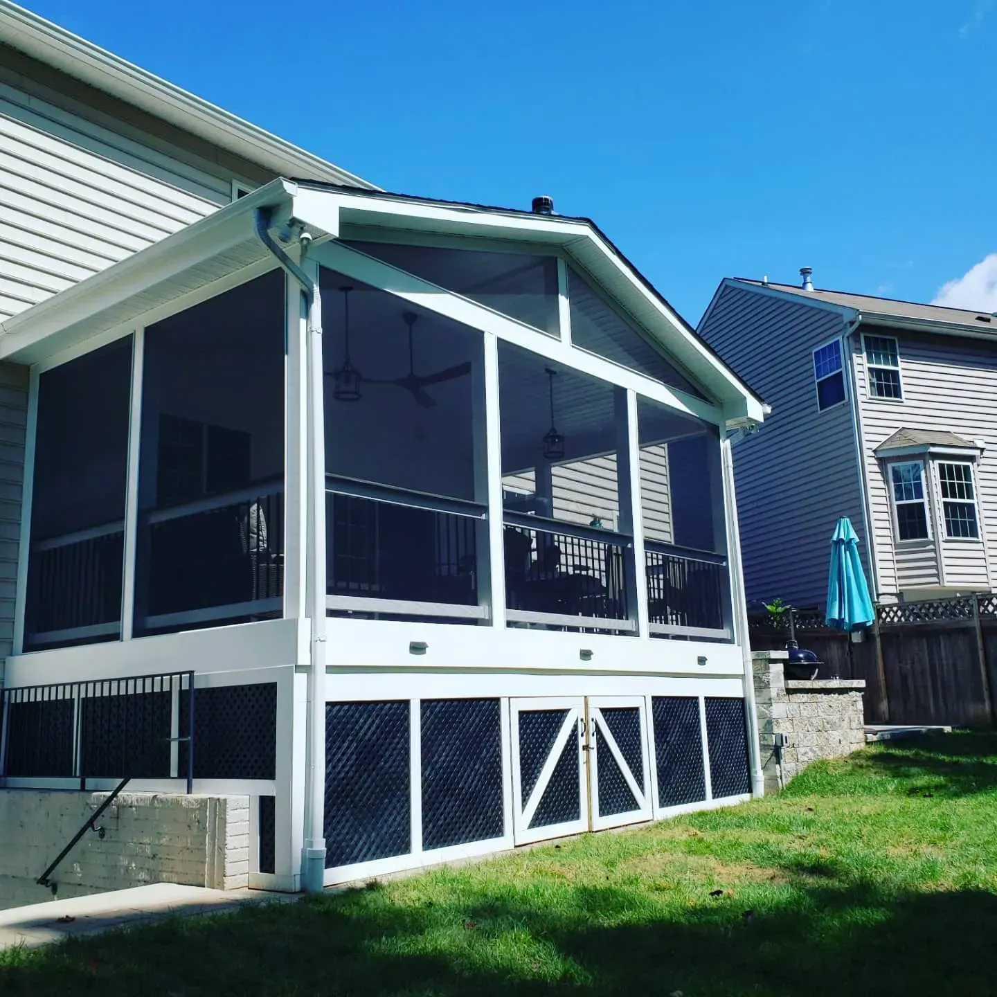 Screened-in porch addition with white frame, black screens. Exterior of a house, sunny day, green lawn.