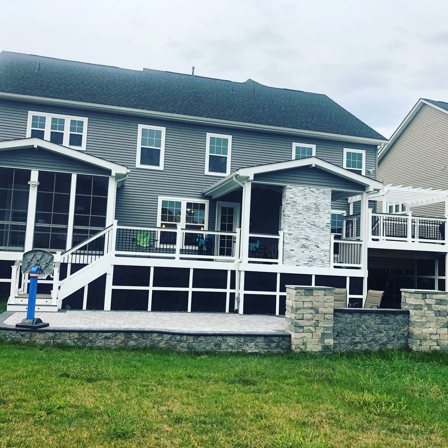 Back of a gray house with a deck, screened porches, and a stone patio on a grassy lawn.