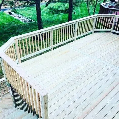 Wooden deck with railing, overlooking a grassy yard and trees.