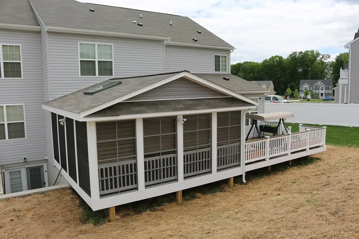 Screened-in porch attached to a two-story house; features a deck, white railing, and gray roof.