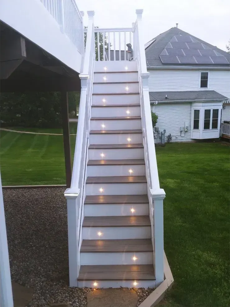 White deck stairs with embedded lights lead down to a grassy yard. A dog sits at the top.