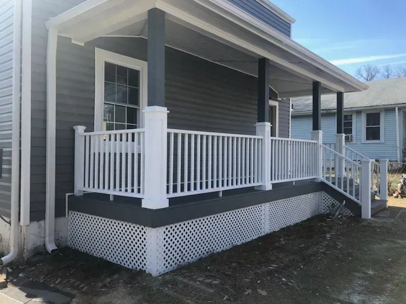 A newly constructed porch with white railing and dark gray siding.
