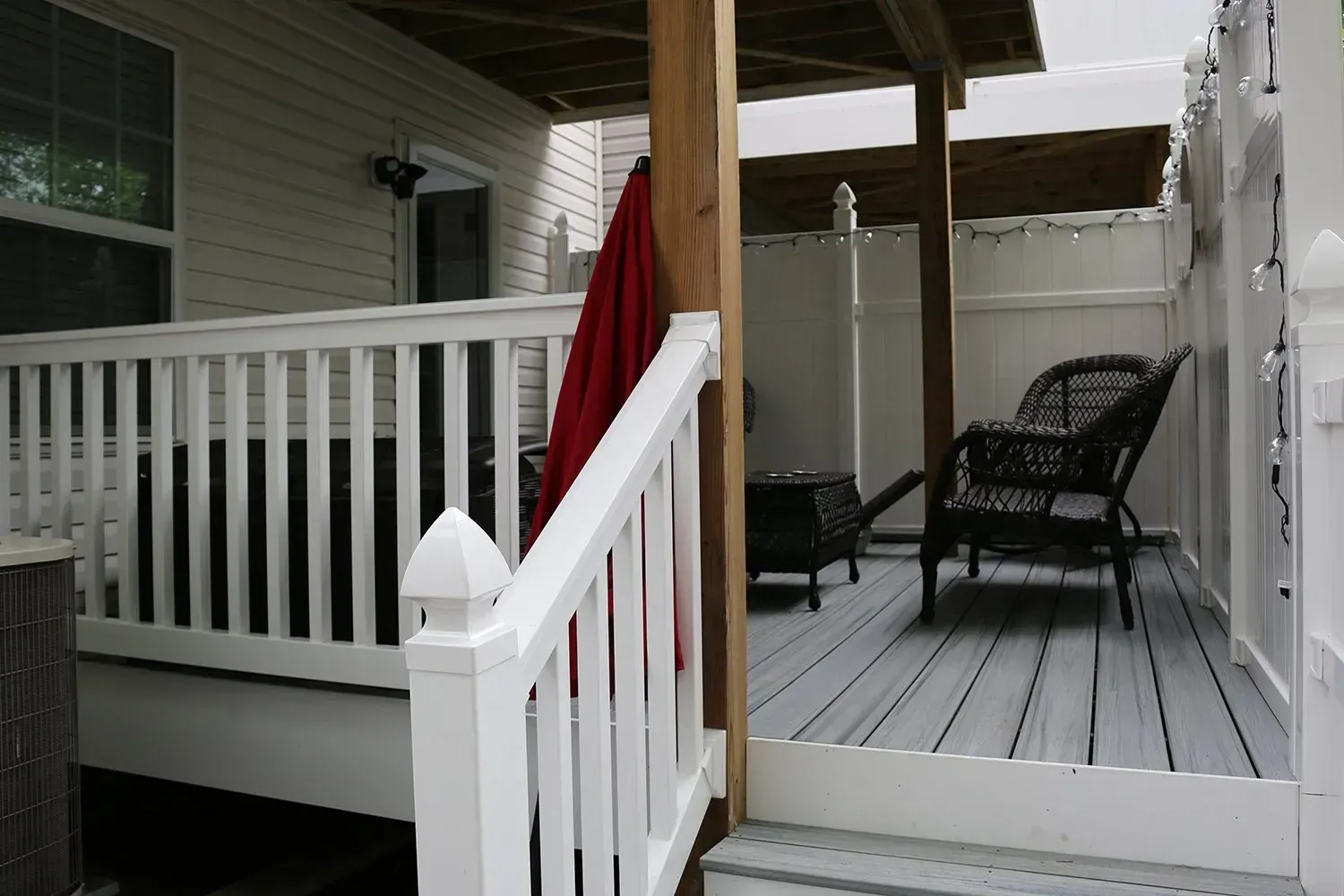 White deck with railing, part of a house. Red fabric, wicker chair, and firepit visible.