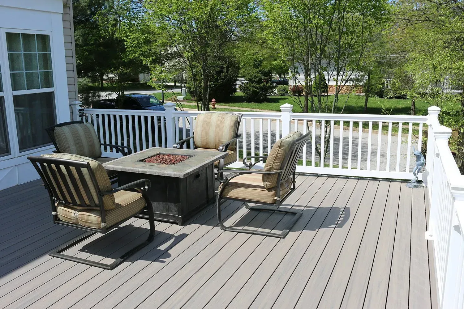 Deck with outdoor seating around a fire pit, white railing, and view of trees.