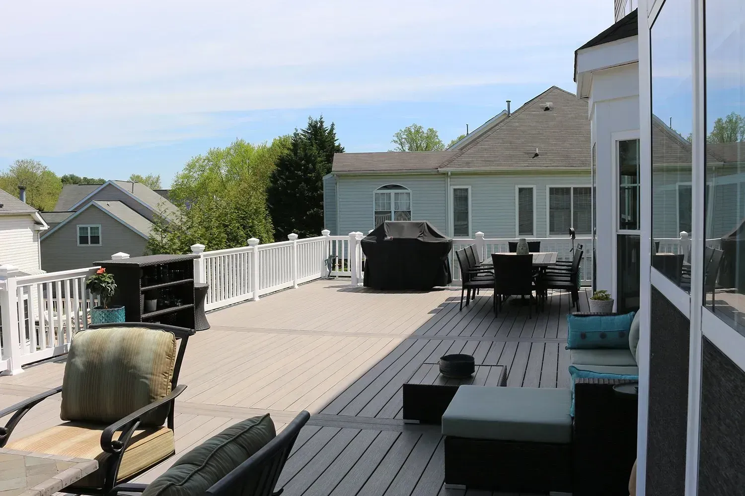 Large wooden deck with outdoor furniture, grill, and a view of neighboring houses.