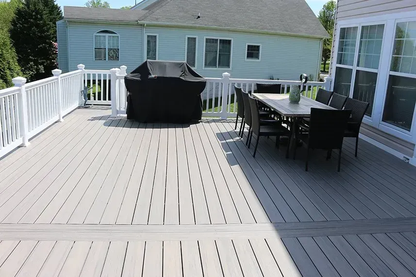 Gray composite deck with white railing, grill, table with chairs, and a house in the background.