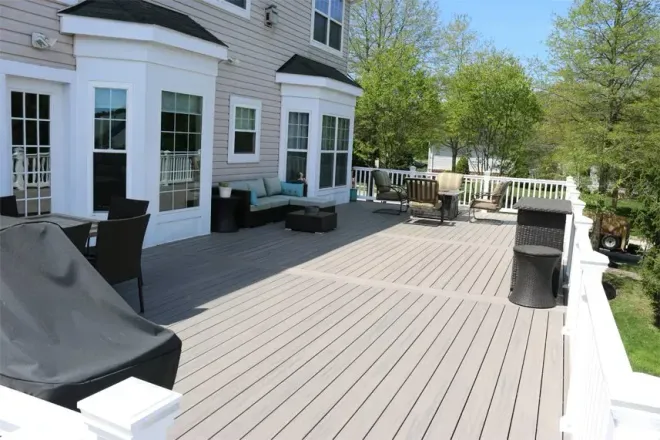A spacious wooden deck on a light-colored house with outdoor seating, overlooking a yard with trees.