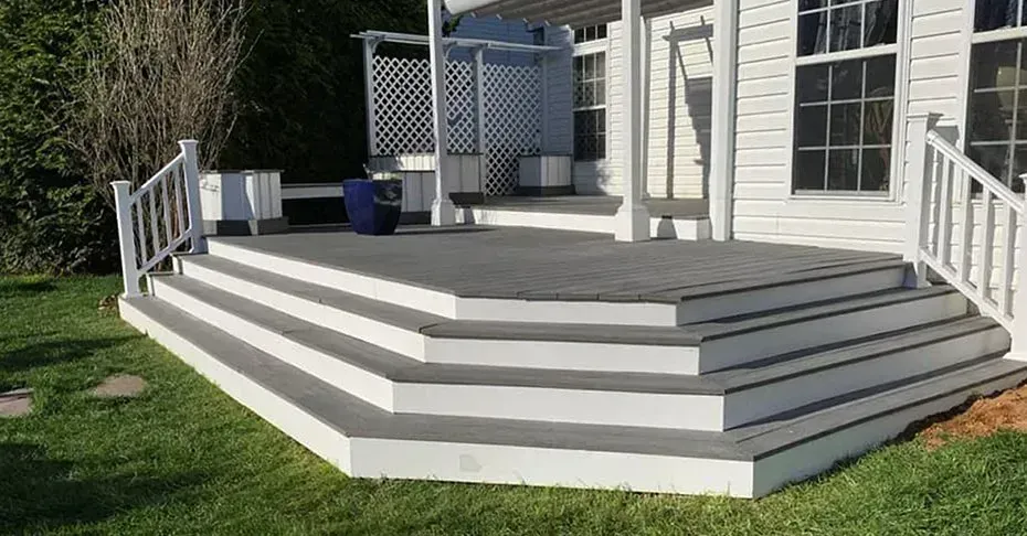 White deck with grey steps and railing, leading up to a white house with windows.