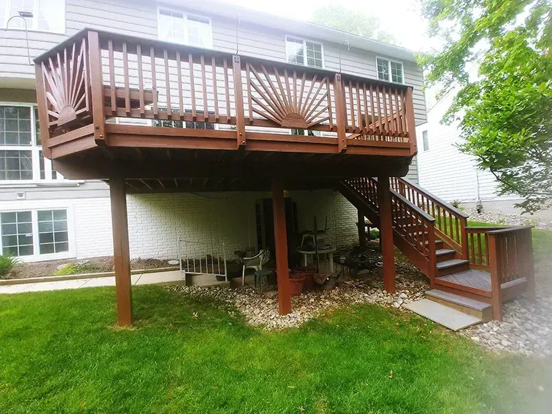 Brown wooden deck with stairs attached to a two-story building.  Green grass and landscaping surround.