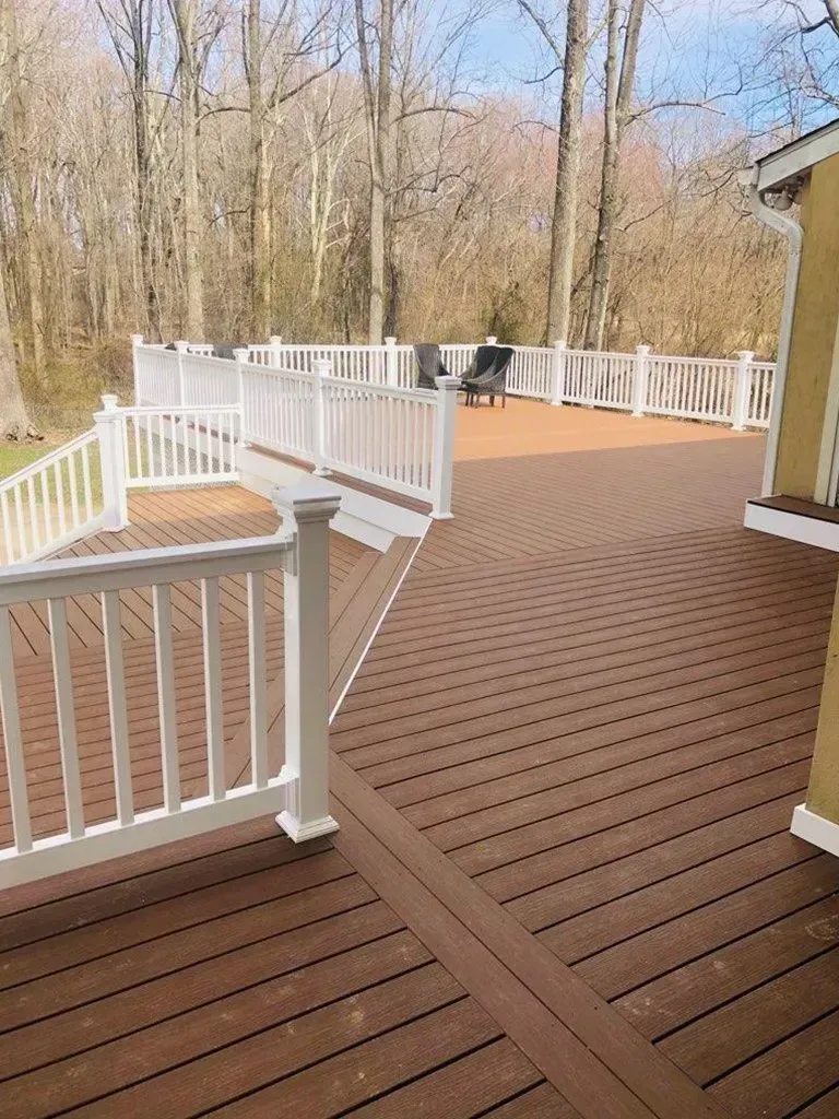 Multi-level wooden deck with white railing, brown decking, surrounded by trees.