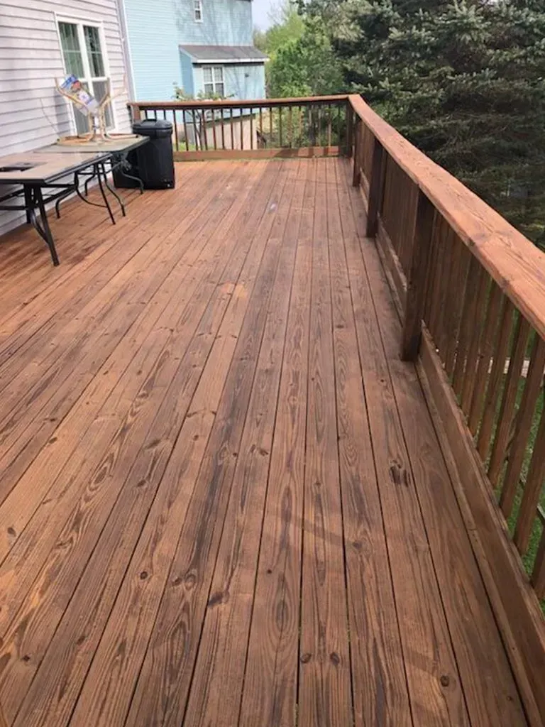 Wooden deck with brown stain and railing, extending from a light-colored house.