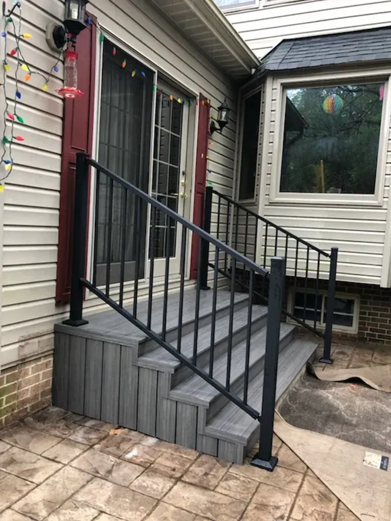 A dark gray deck with black handrails and steps leads to a glass sliding door. Exterior of a house.