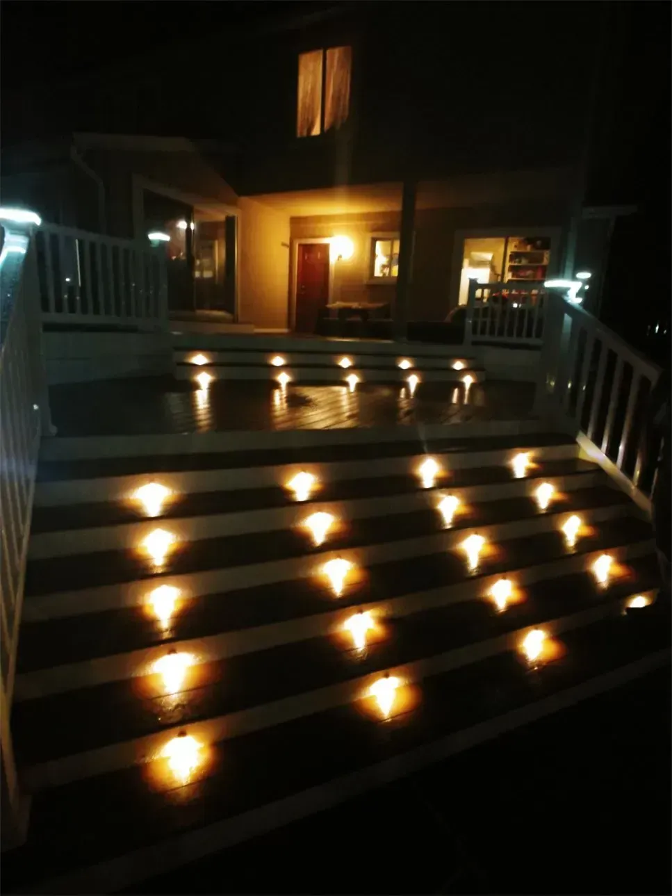 Illuminated outdoor staircase at night, leading to a house. Warm lights glow on each step.