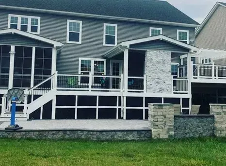 Back exterior of a gray house with a deck, screened porch, and stone patio.