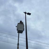 Person in a bucket lift working on a street light against a cloudy sky.