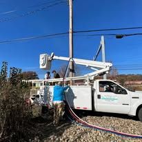 Utility truck with a bucket lift, workers, and a utility pole.