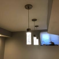 Three pendant lights with cylindrical glass shades hanging from a ceiling in a room.