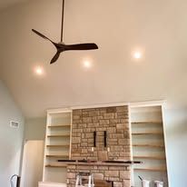 A room with a fireplace, built-in shelves, ceiling fan, and recessed lighting.