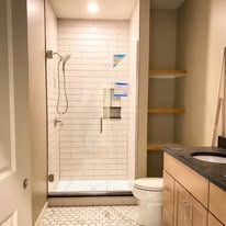 Bathroom with a glass shower, white subway tile, and a wooden shelf.