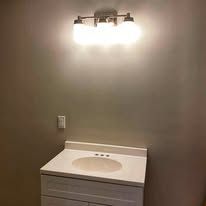 Bathroom vanity with sink under a three-bulb light fixture on a gray wall.