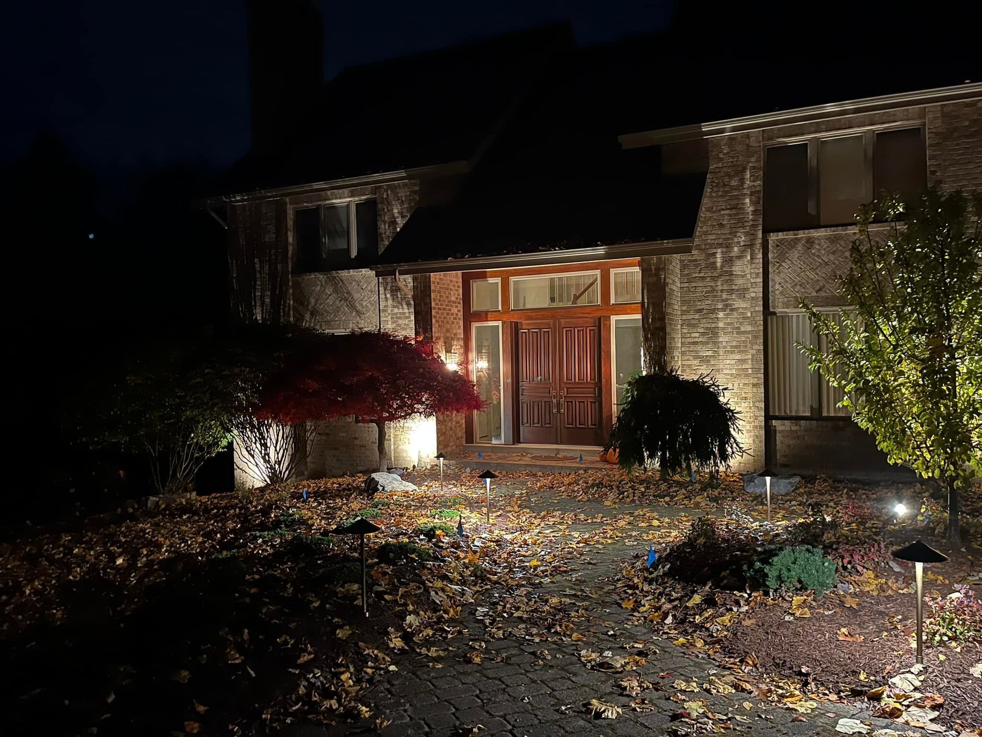 Two-story brick house at night, lit by landscape lights.