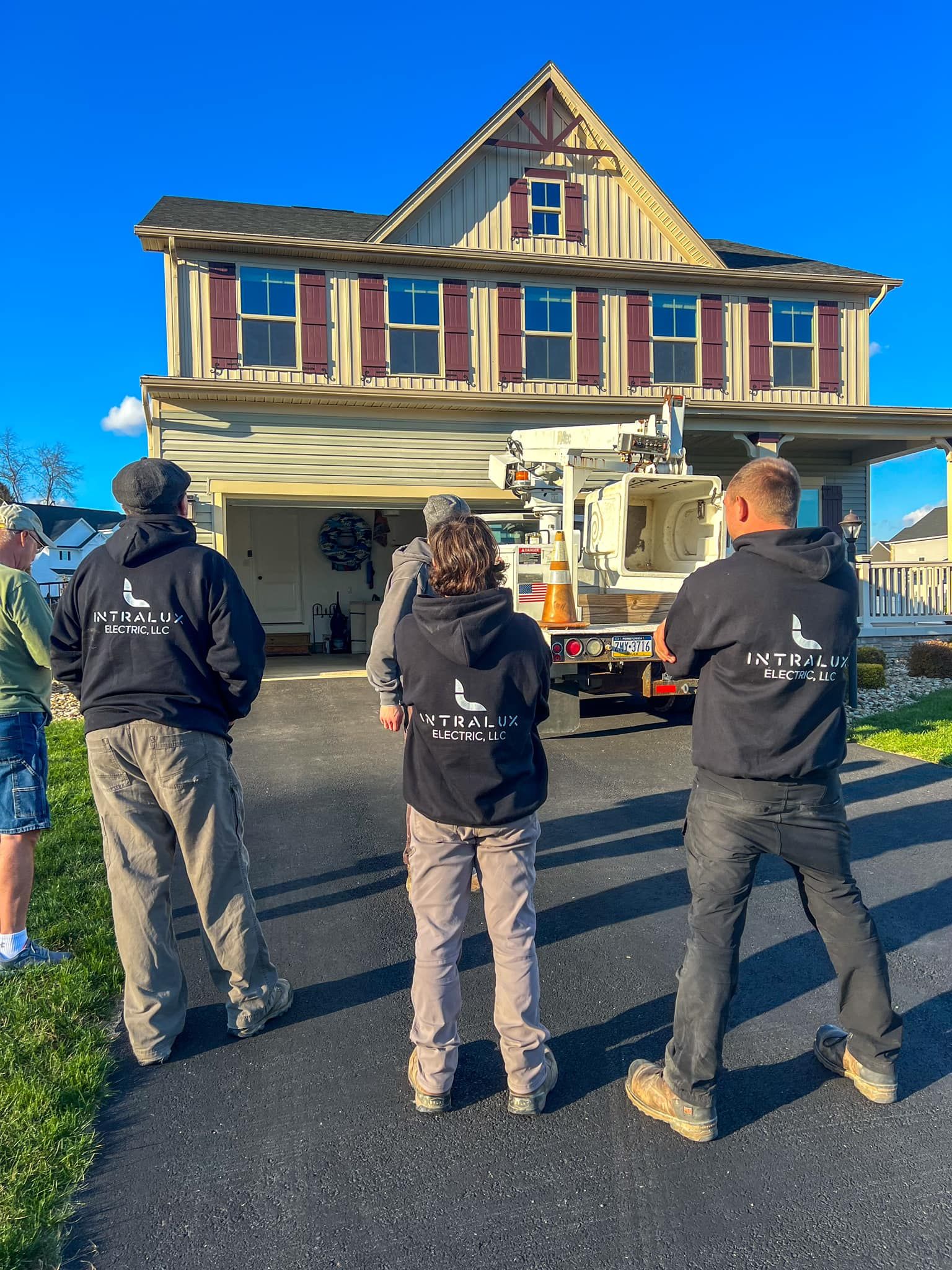 Three people in black hoodies with a logo inspect a house with a lift truck, sunny day.