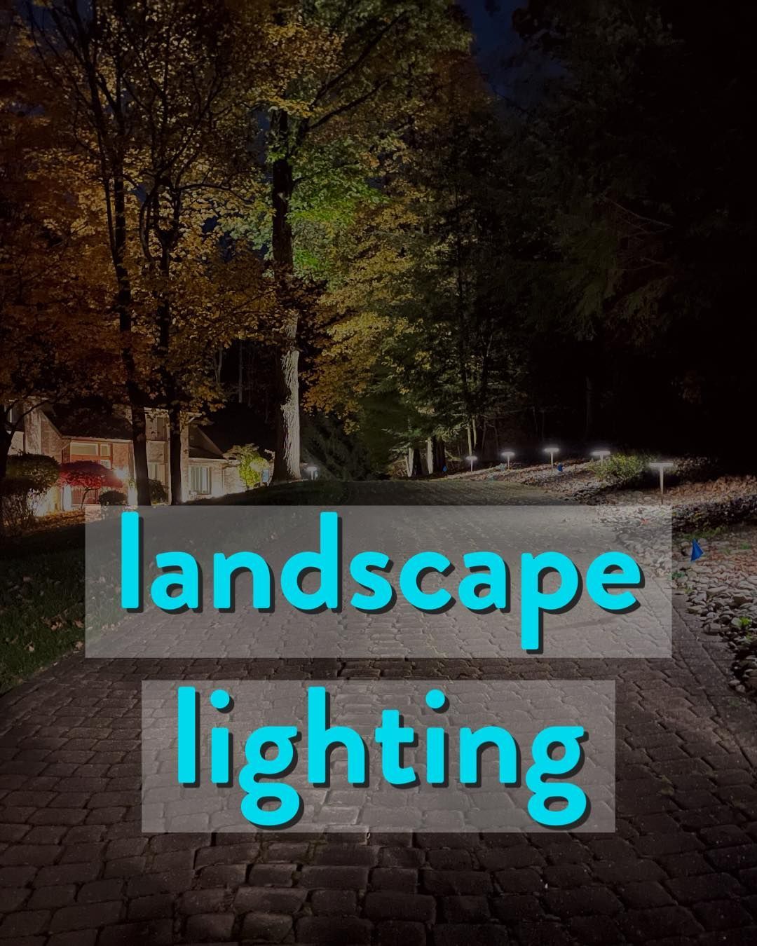 Cobblestone pathway lit by landscape lights; trees with fall foliage in the background.