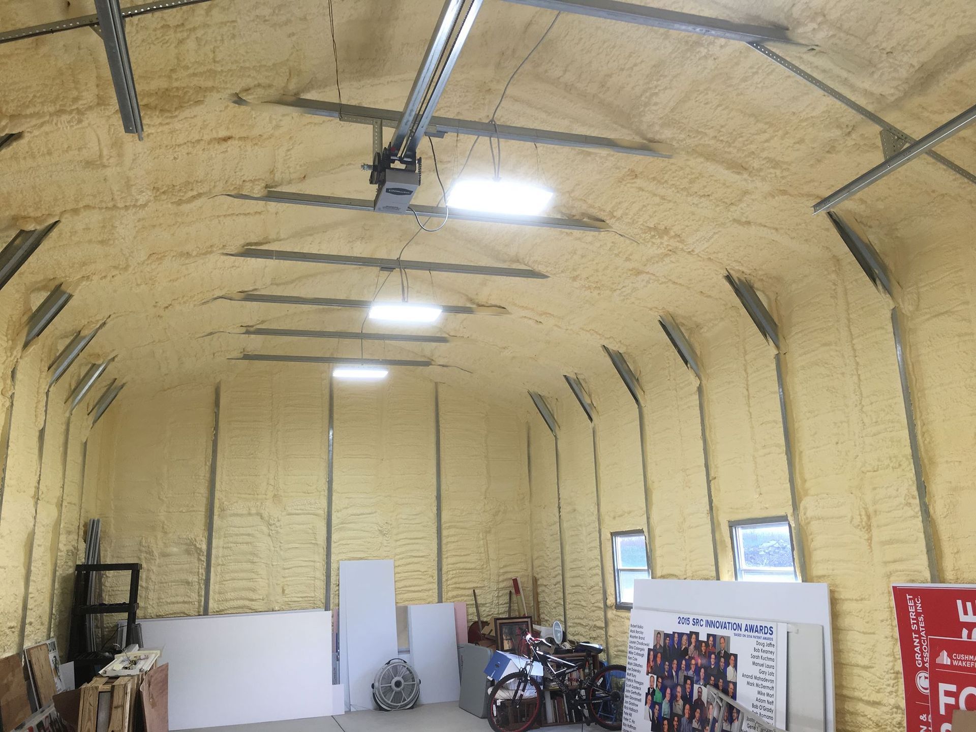Interior of a building with spray foam insulation on the walls and ceiling, garage door opener visible.