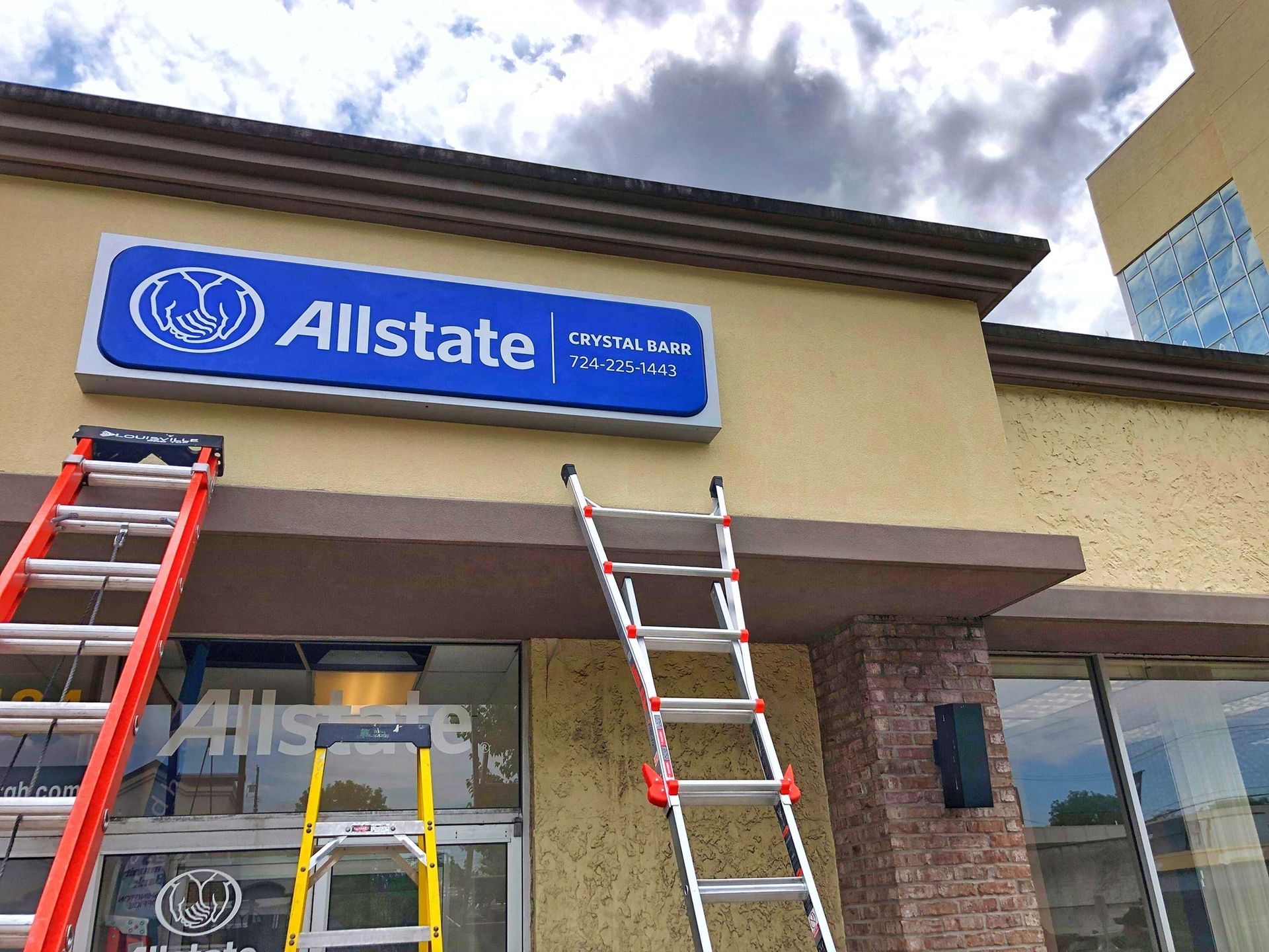 Allstate storefront sign above entrance, with three ladders set up for maintenance under a cloudy sky.