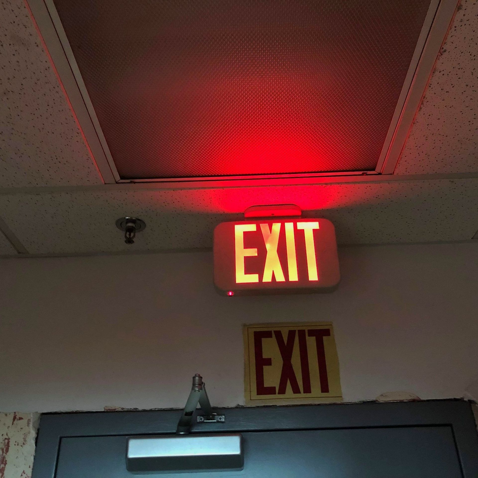 Red EXIT sign above a door, illuminated, with a second faded EXIT sign below.
