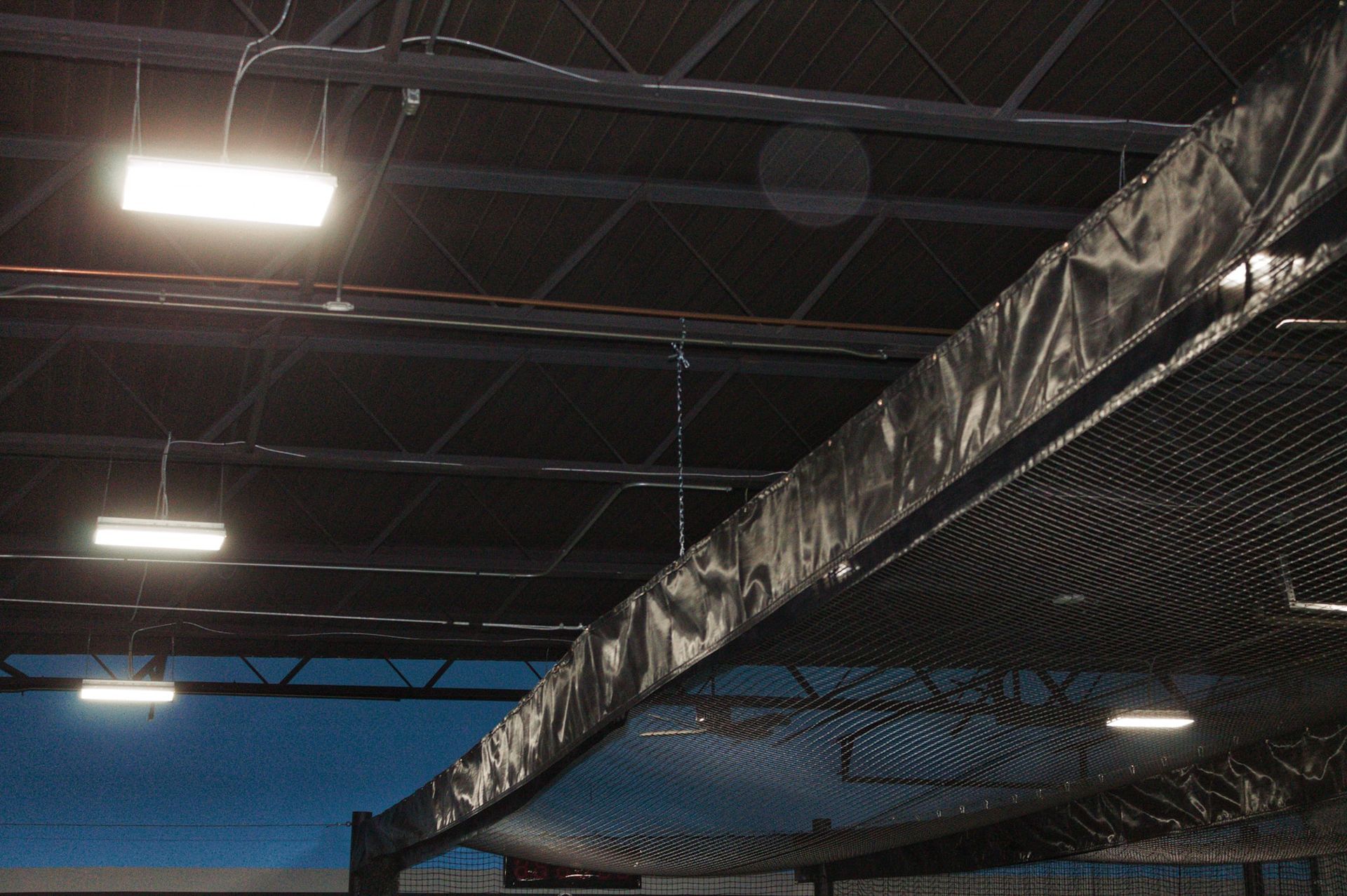 Black netting and fabric attached to ceiling supports in an indoor facility; bright lights.