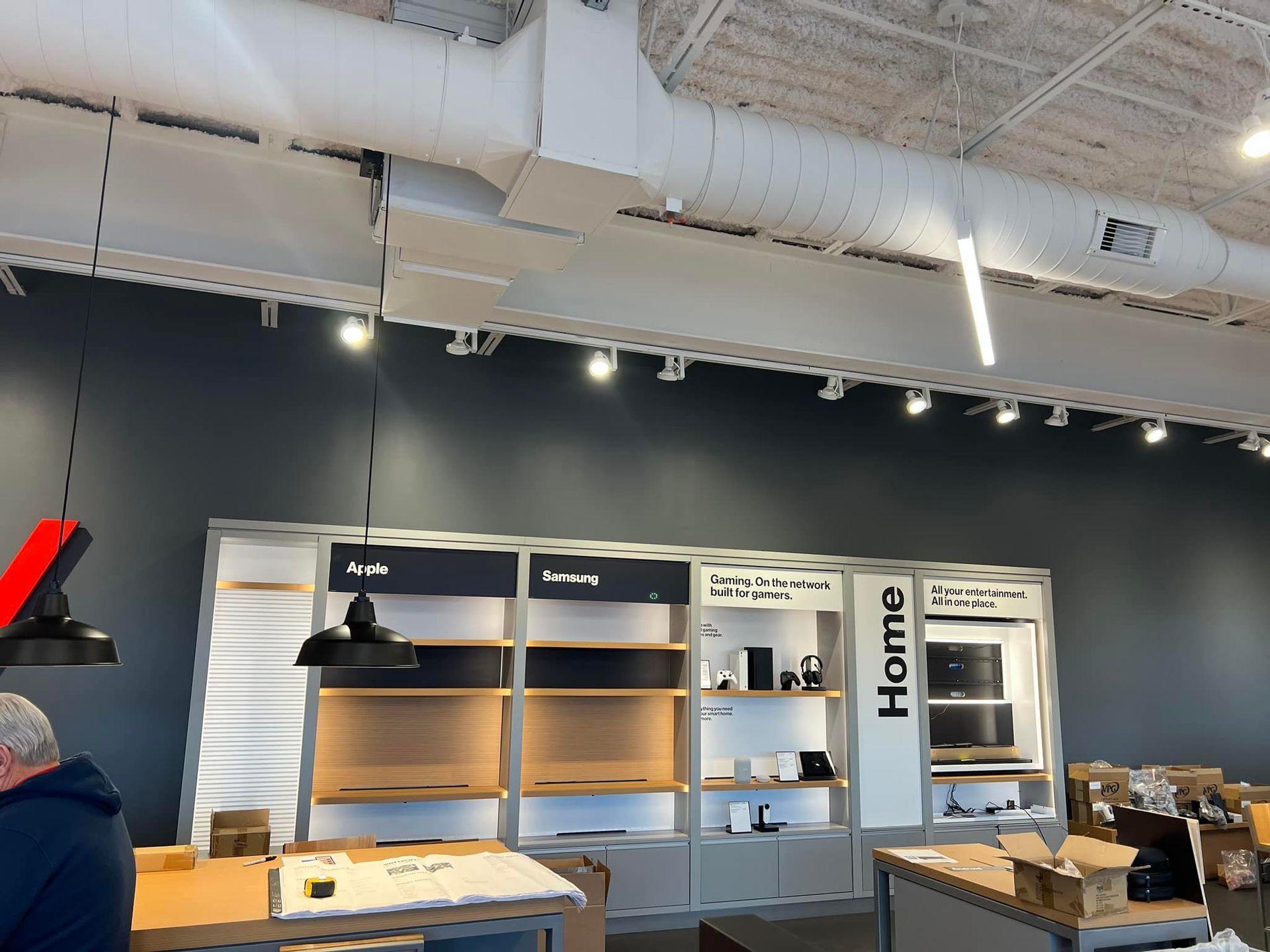 Interior shot of a retail store with shelving displays, a person, and overhead lighting fixtures.