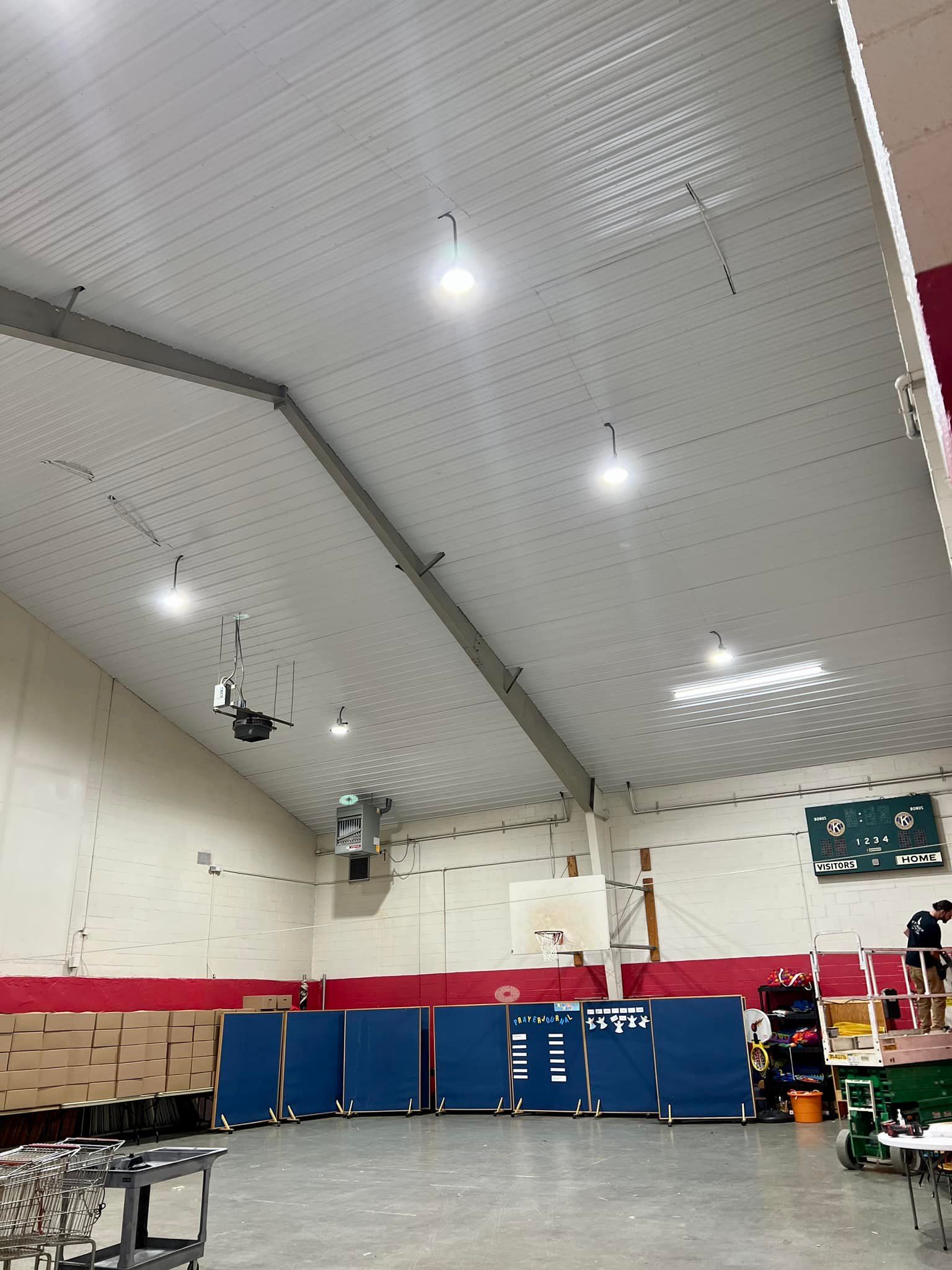 Brightly lit indoor space, possibly a gymnasium, with white walls and ceiling, blue dividers, and basketball hoop.