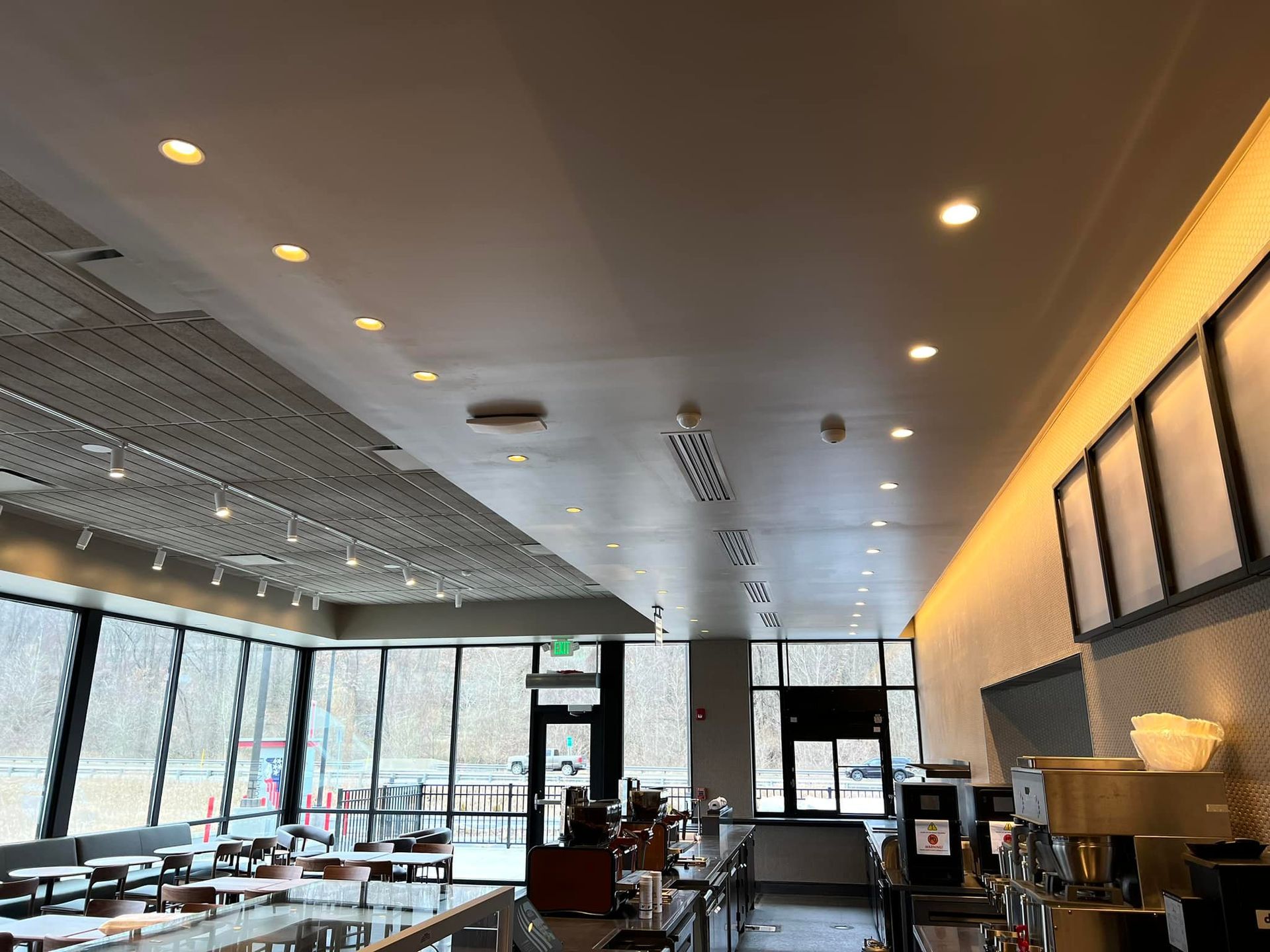 Interior of a brightly lit coffee shop. Windows on one side, service counter on the right with menu boards.