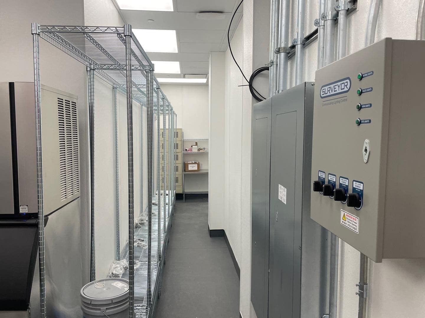A narrow hallway with shelving, electrical panels, and metal conduit on the walls.