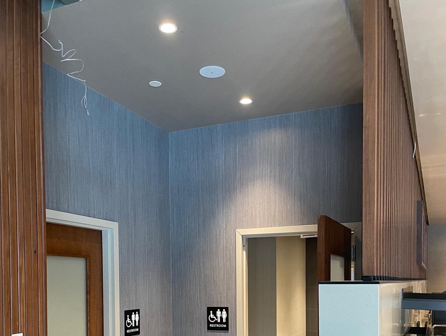 Restroom entrance with textured blue walls, recessed lights, and wooden accents.