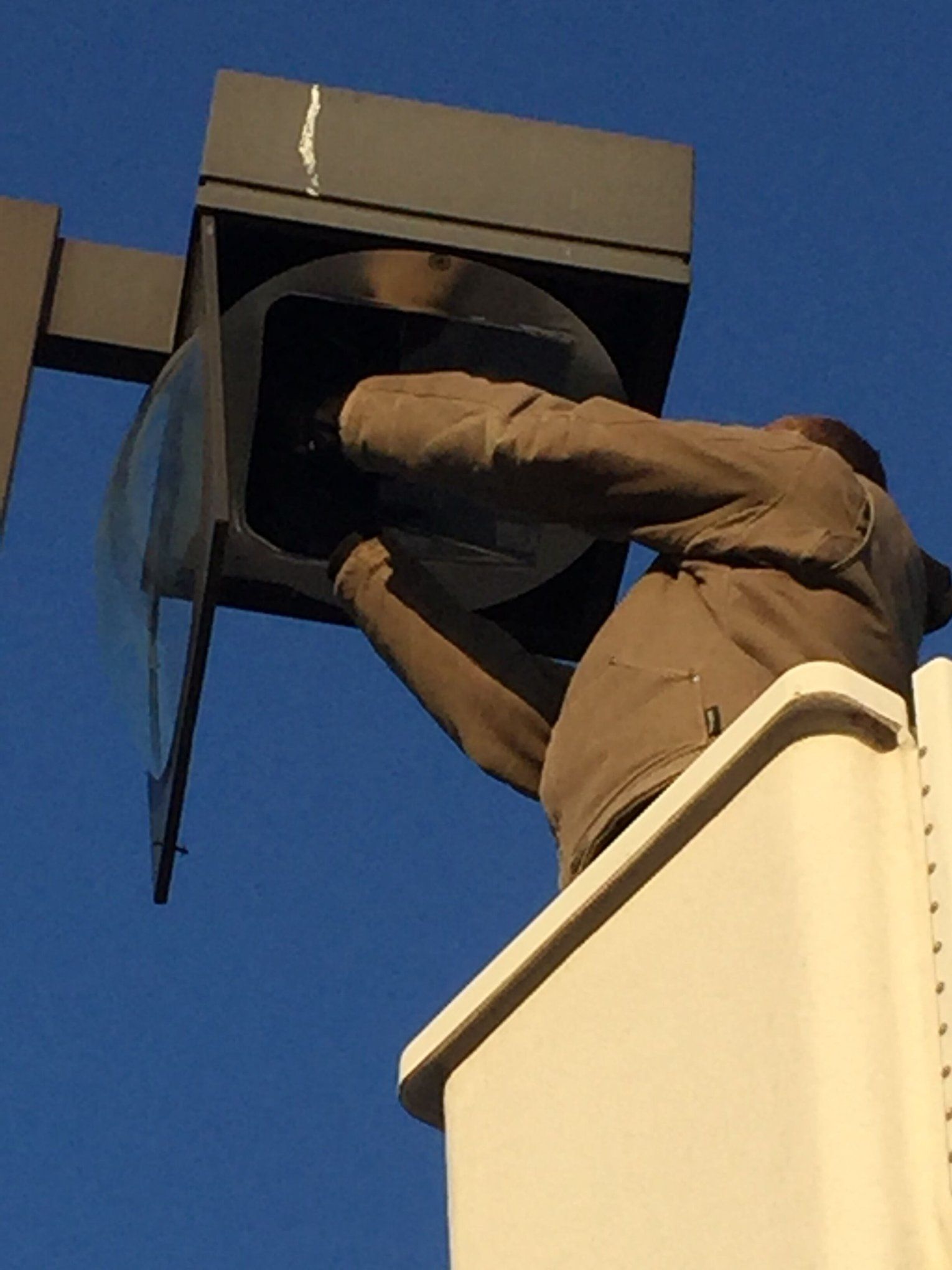 A worker in a bucket truck repairs a streetlight against a blue sky.