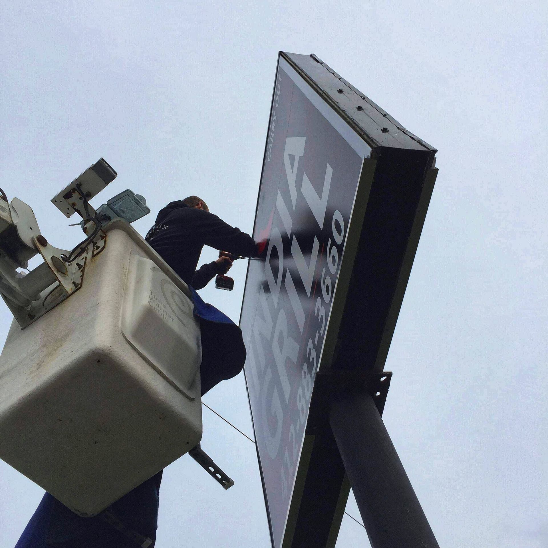 Person in lift bucket installing a large sign outdoors.