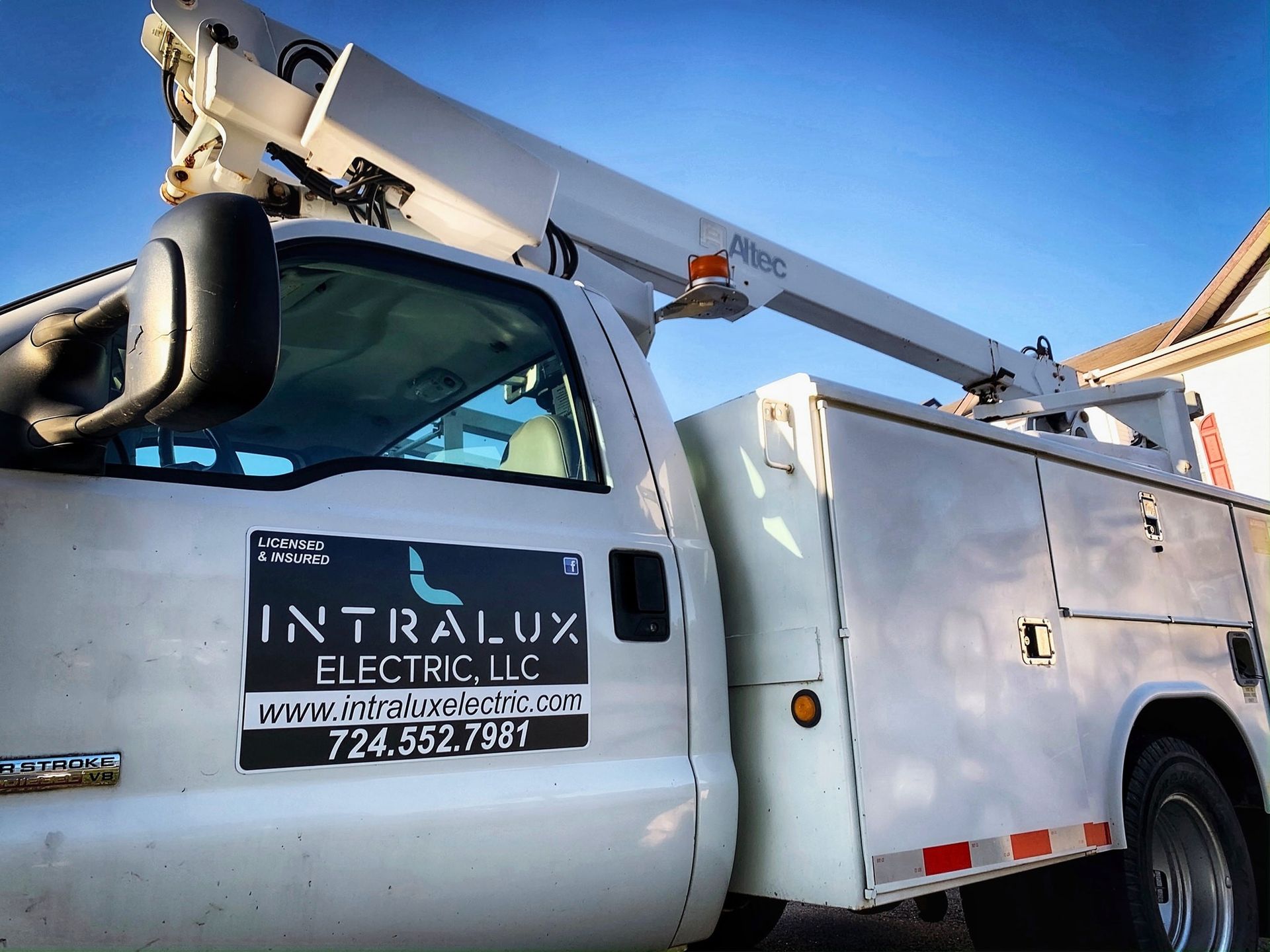 White Intralux Electric truck with a boom lift parked outside.