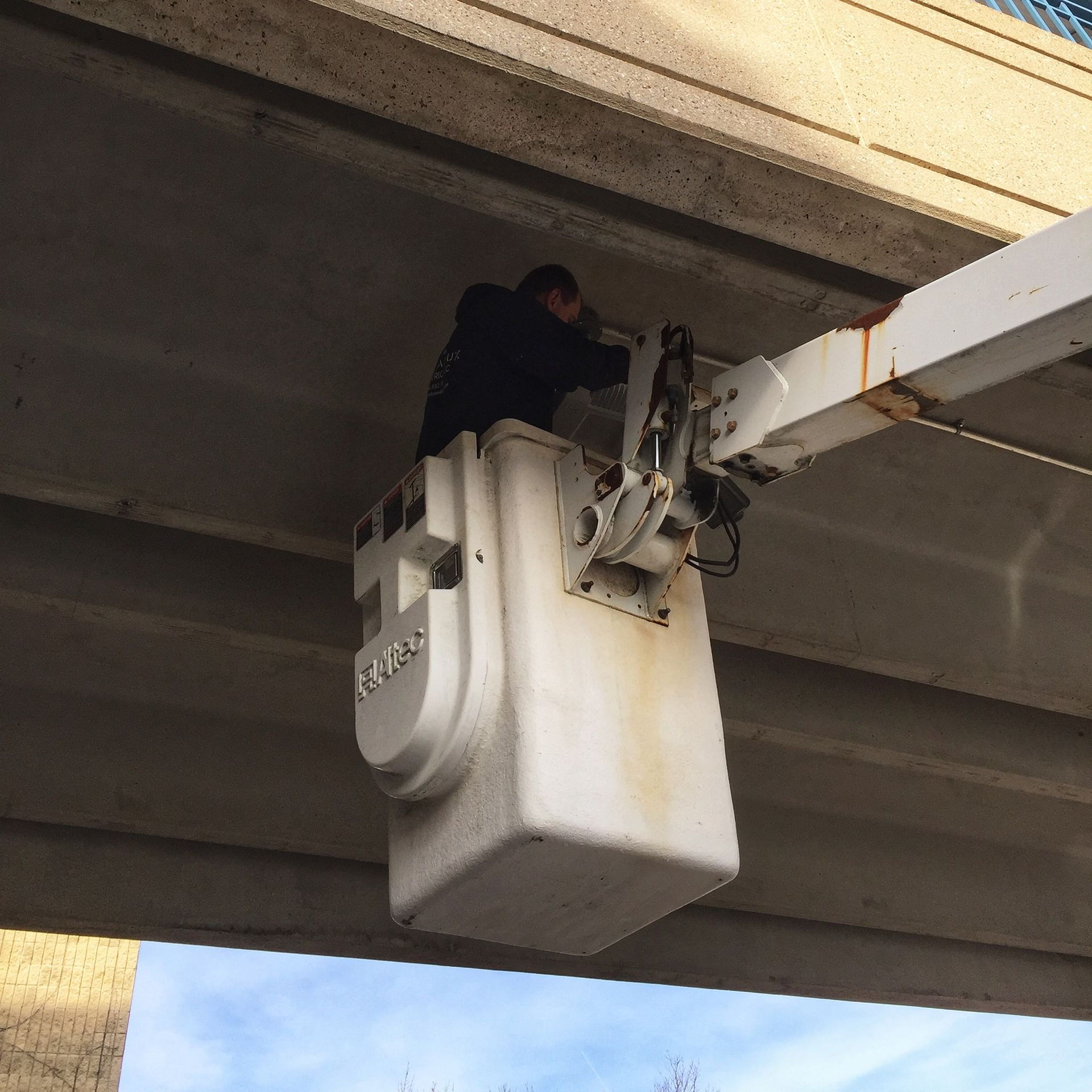 Man in bucket lift working under a concrete bridge, possibly on lights or infrastructure.