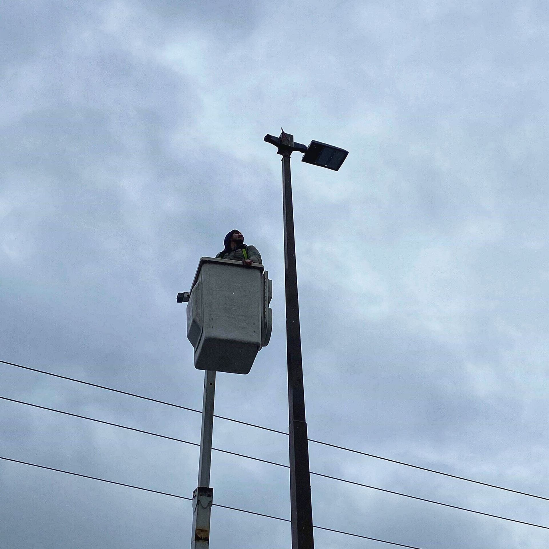 Person in bucket lift repairing a streetlight against a cloudy sky.