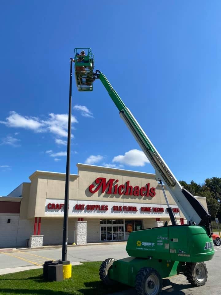 Man in lift working on pole in front of Michaels craft store, sunny day.