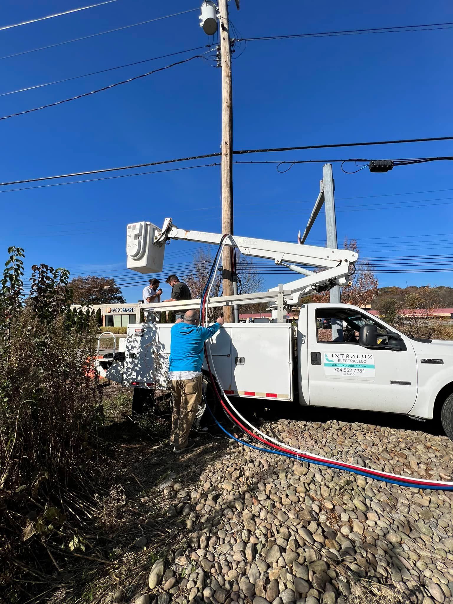 Utility truck with raised boom working on a power pole. Person near truck, overhead power lines, clear blue sky.