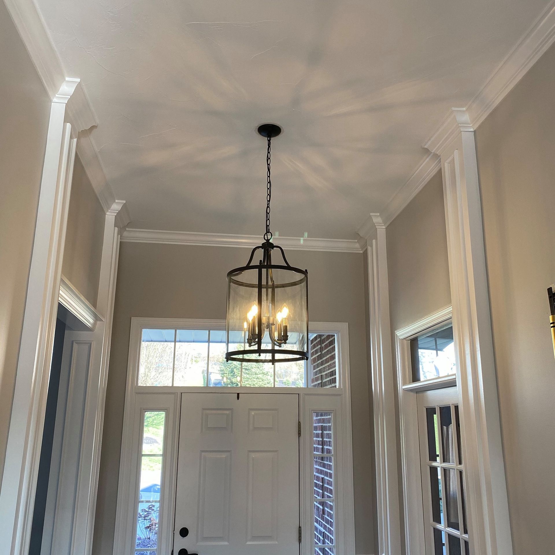 Hallway with white trim, a black chandelier, and a white front door.