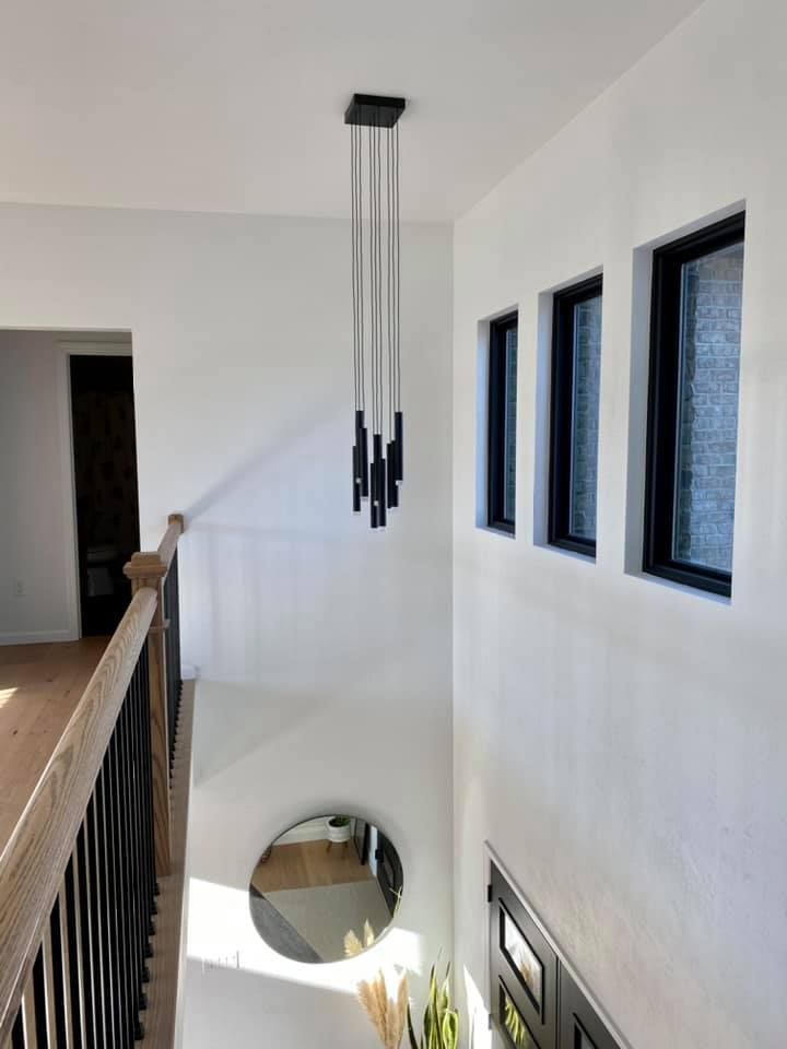 Modern hallway with black light fixture, windows, and round mirror.
