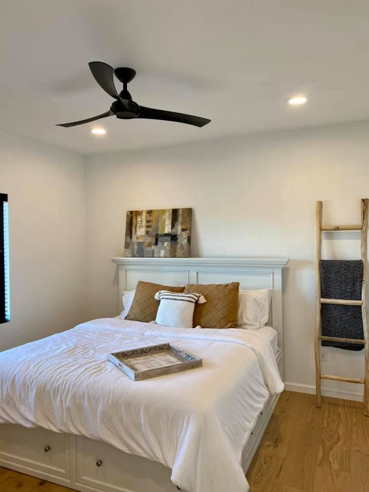 Bedroom with white walls, a bed with brown and white pillows, and a wooden ladder.
